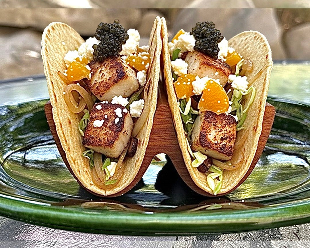 Two tacos with seafood and vegetables on a green plate with a blurred background