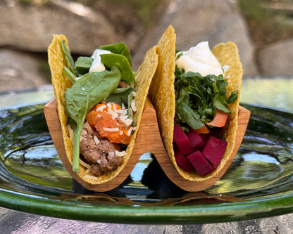 Two tortilla tacos with different fillings on a green plate in a beautiful wood taco holder outdoors.
