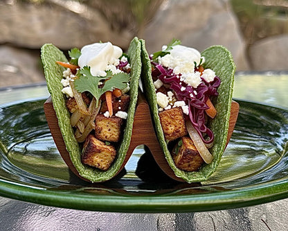 Two tacos on a green plate with a blurred natural background