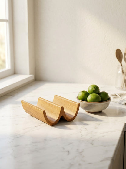 Solid oak double taco holder on marble kitchen counter beside a ceramic bowl of fresh limes