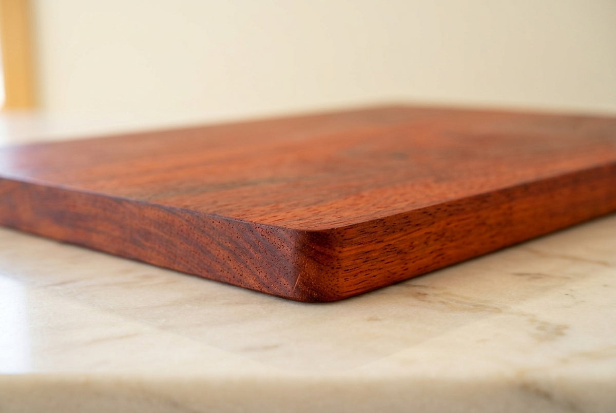 Close up of padauk cutting board corner showing open wood grain pores, rounded corner, crisp edge and solid one inch thickness