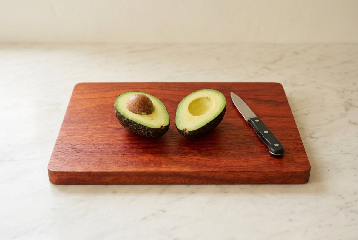 Handmade padauk cutting board with ripe avocado cut in half and paring knife on marble counter