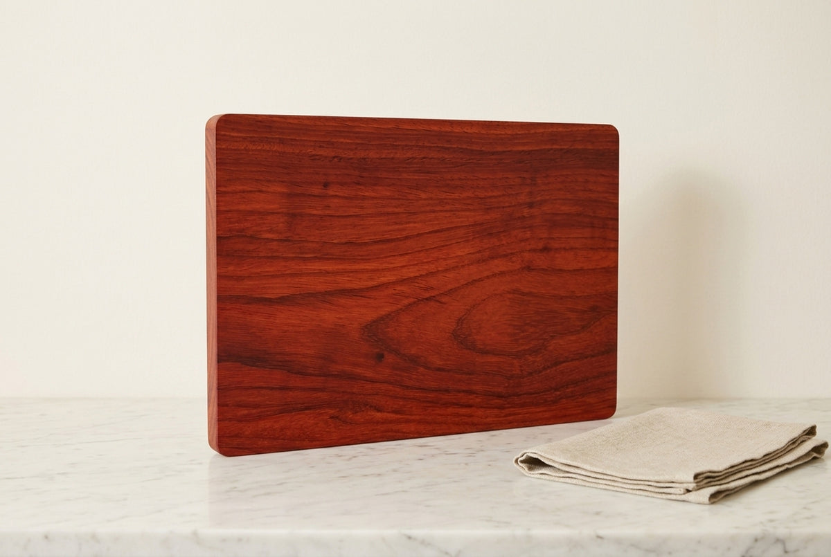 Single slab padauk cutting board standing upright showing full red orange grain face with folded linen tea towel on marble