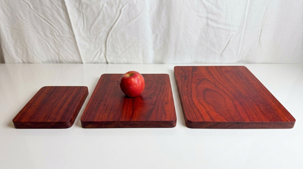 Padauk cutting boards in small, medium and large sizes side by side with red apple on medium board for scale