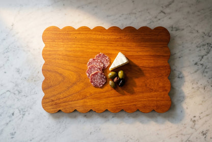 Overhead padauk scalloped charcuterie board minimal salami brie olives sparse elegant lots of empty board showing on marble