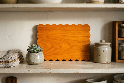 Padauk scalloped charcuterie board on kitchen shelf with succulent ceramic jar warm home decor display editorial