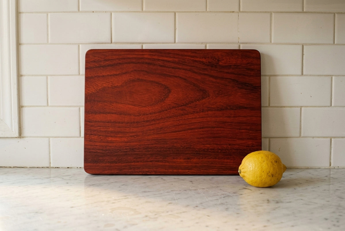 African padauk cutting board standing upright against subway tile backsplash showing vivid red orange grain pattern and board thickness