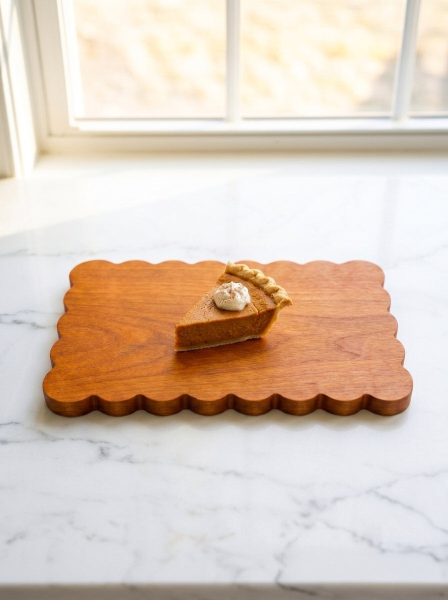 Padauk scalloped charcuterie board with a single slice of pumpkin pie on white marble counter